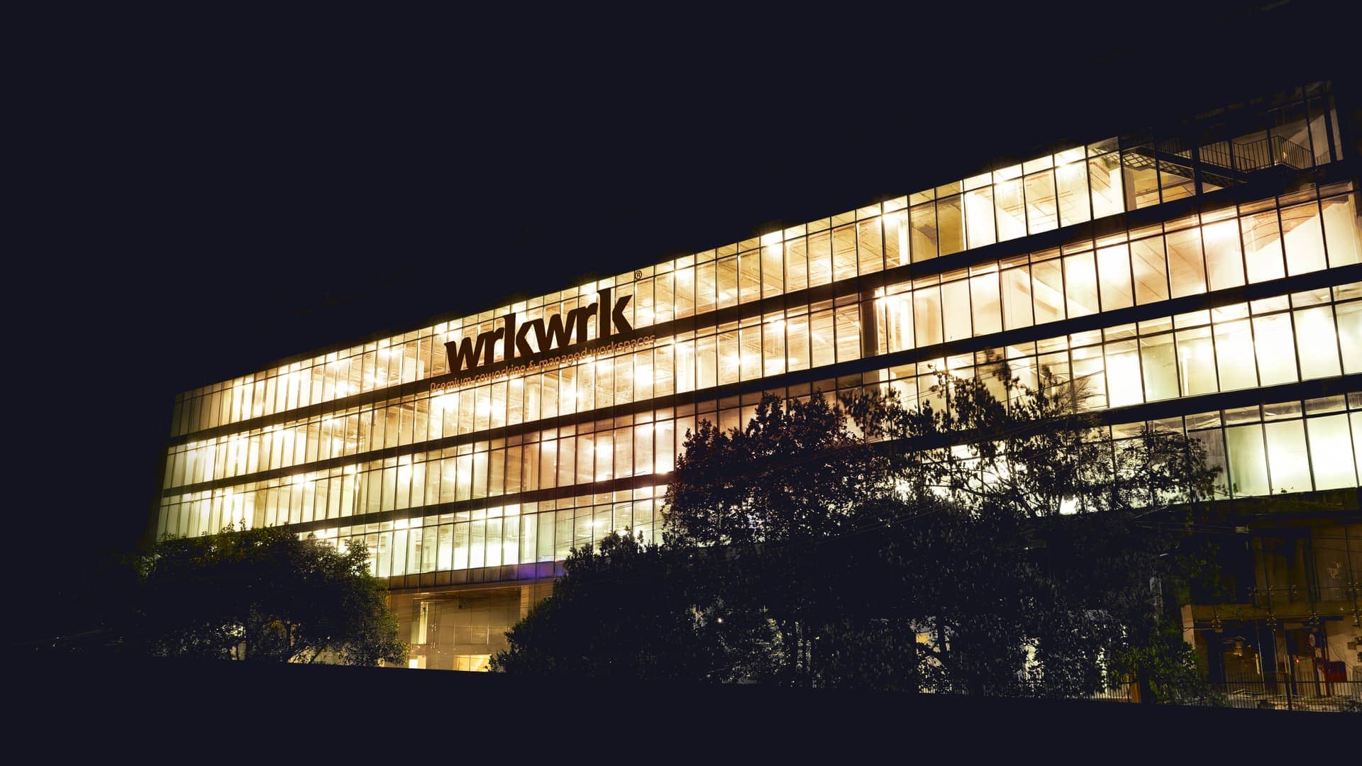 The wrkwrk building at night, its glass frontage lit from within across four floors